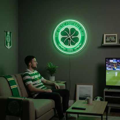 A man holding a circular The Celtic Football Club crest LED neon sign featuring the traditional four-leaf clover logo glowing in a vibrant green light