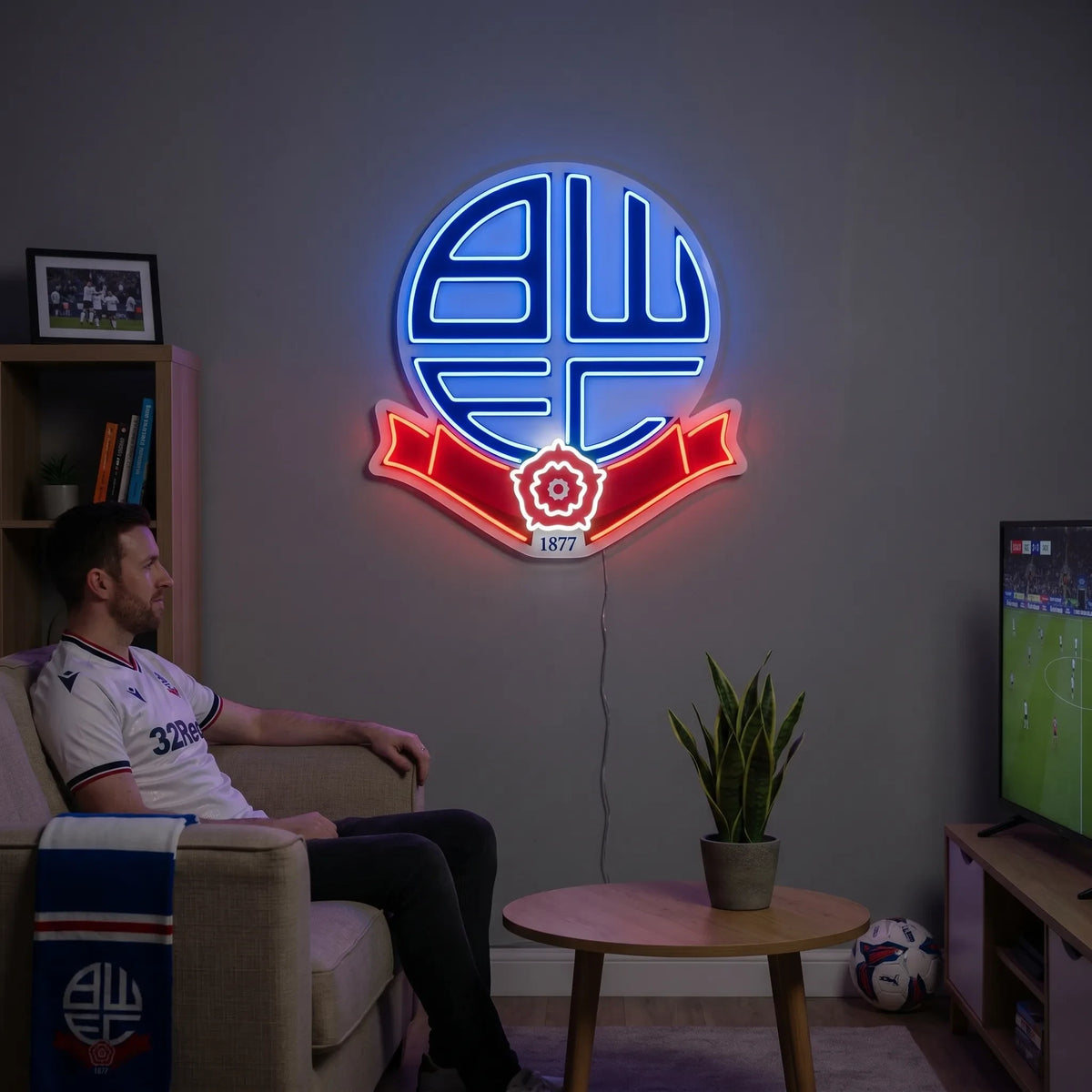 A man holding a circular Bolton Wanderers FC football club crest LED neon sign featuring the BWFC initials and the Red Rose of Lancashire ribbon glowing in blue and red light