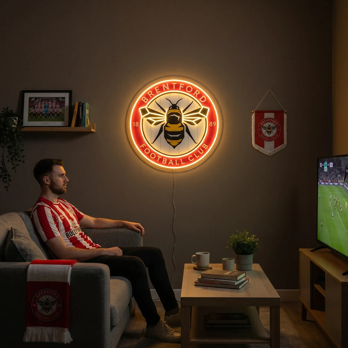 A man holding a circular Brentford FC football club crest LED neon sign featuring the iconic bee logo glowing in warm yellow and red light