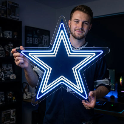 A man holding a large star-shaped Dallas Cowboys NFL football team logo LED neon sign featuring the iconic blue and white layered star design glowing in vibrant royal blue and bright white light