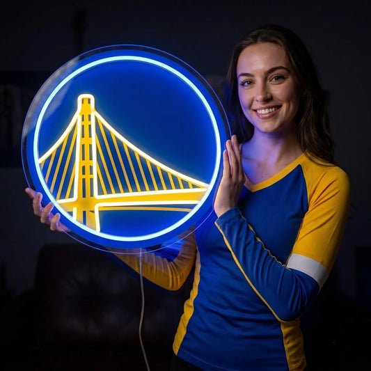 A smiling woman holding a round glowing blue and yellow Golden State Warriors NBA basketball team LED neon sign featuring the Bay Bridge logo