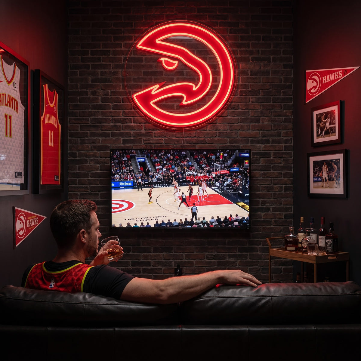Atlanta Hawks LED neon sign above a TV in a man cave with framed jerseys, as a fan watches basketball from the sofa