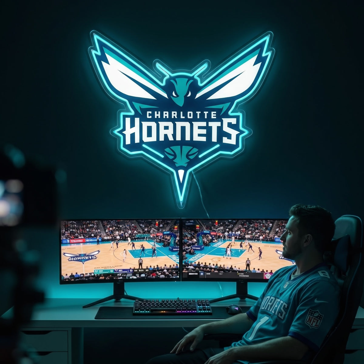 Charlotte Hornets LED neon sign glowing teal above dual monitors showing basketball in a gaming room