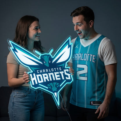 Woman and a man in a Hornets jersey holding a glowing Charlotte Hornets LED neon sign together