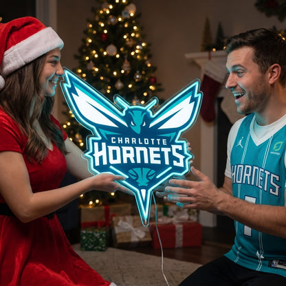 Woman in a Santa hat giving a Charlotte Hornets LED neon sign as a Christmas gift beside a decorated tree