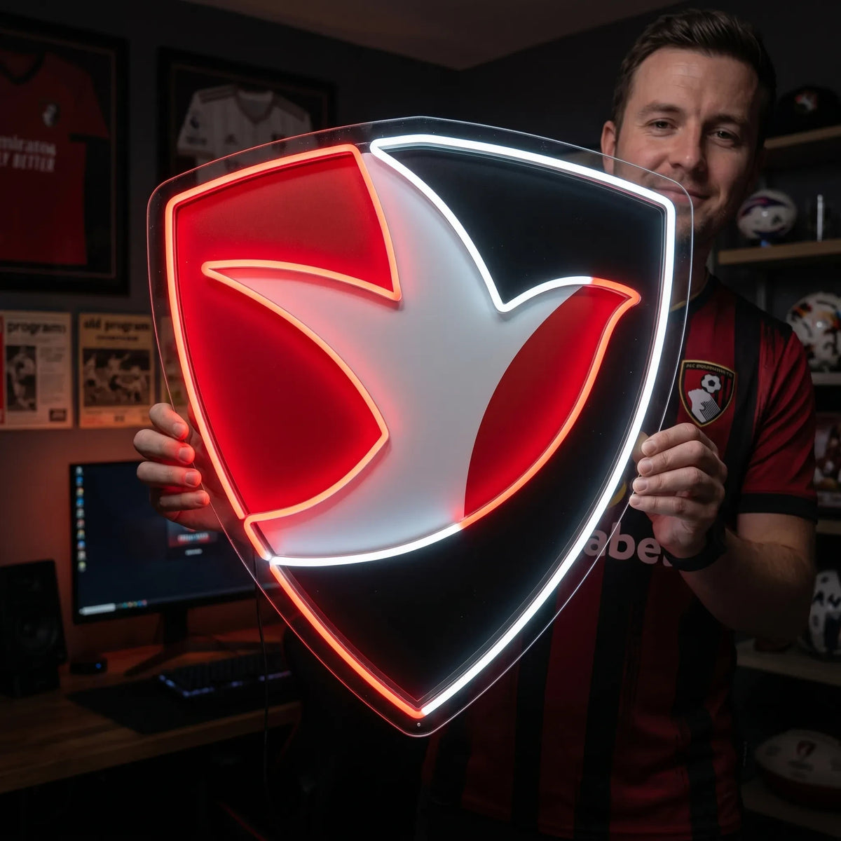 Cheltenham Town FC LED neon sign - A man holds a glowing red, black and white robin shield crest neon sign in a fan room.