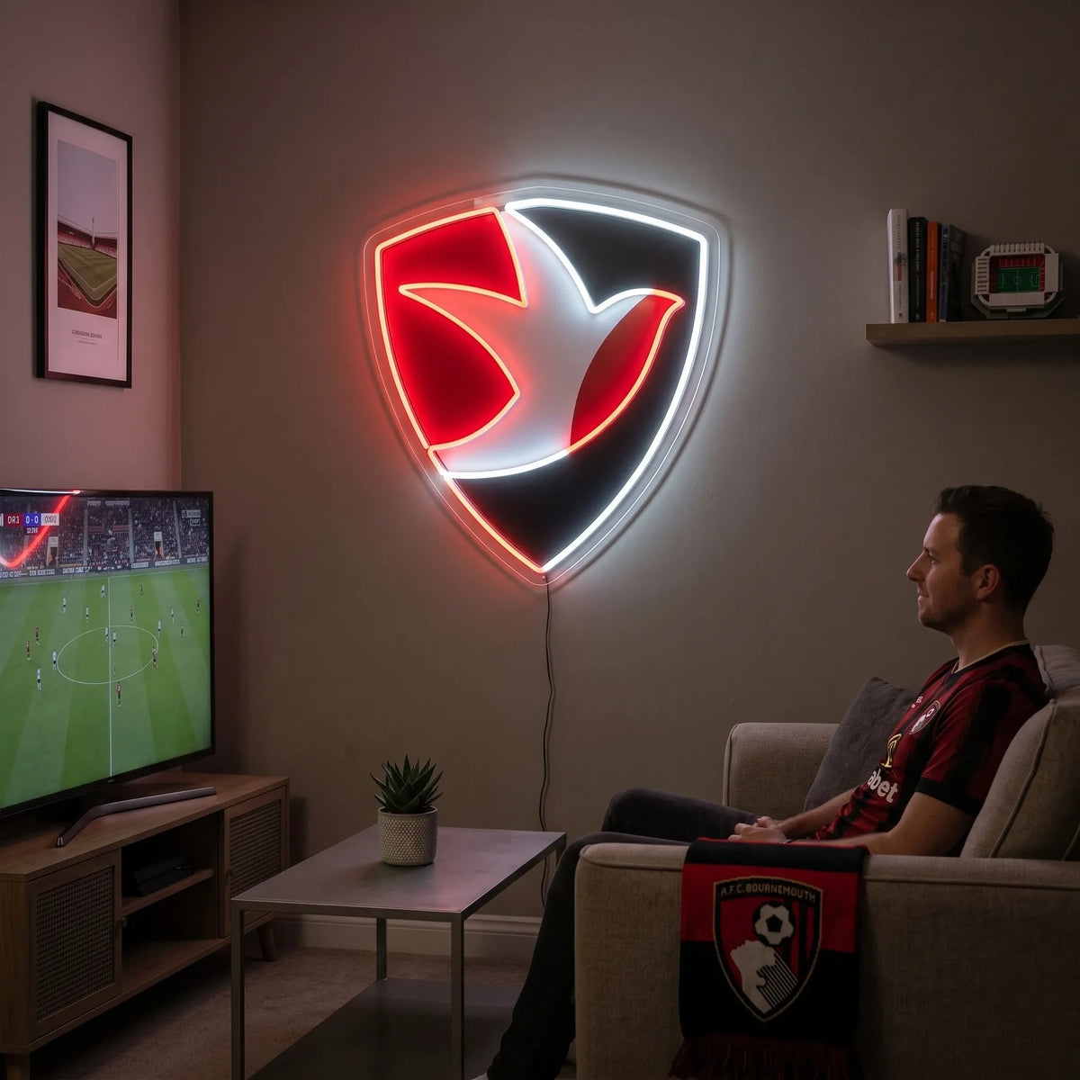 Cheltenham Town FC LED neon sign - A fan relaxes on a sofa watching a football match on TV beside a glowing red, black and white robin shield crest neon sign on the wall.