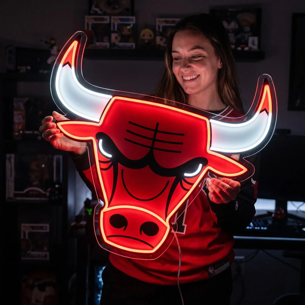 Chicago Bulls LED neon sign - A smiling woman holds a red and white Chicago Bulls logo neon sign in a room with collectibles.