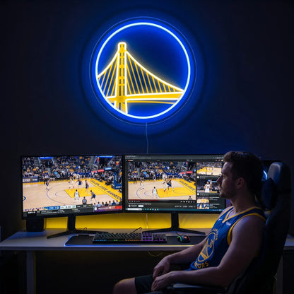 Golden State Warriors LED neon sign - A fan in a Warriors jersey watches basketball on dual monitors beneath a glowing blue and yellow Golden State Warriors logo neon sign.