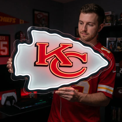 Kansas City Chiefs LED neon sign - A man in a red Kansas City Chiefs jersey holds a large, illuminated NFL sign shaped like the Chiefs arrowhead logo, featuring the red and gold KC logo on a glowing white background.