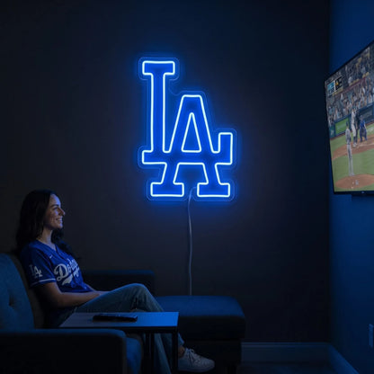 Los Angeles Dodgers LED neon sign - A woman relaxes on a couch in a dark room beside a glowing blue LA Dodgers logo neon sign and a TV showing baseball.