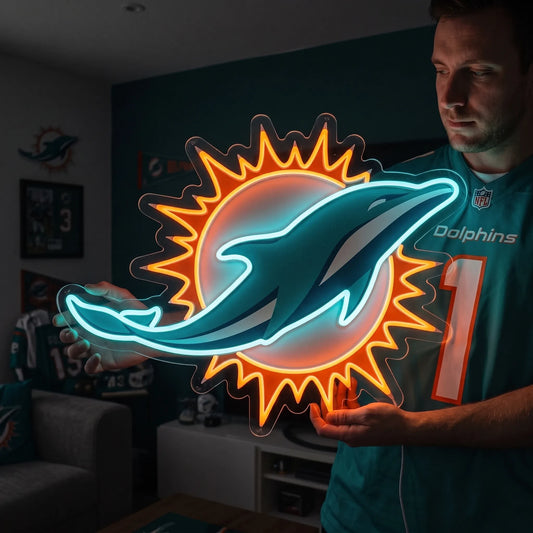 Miami Dolphins LED neon sign - A man in a teal Miami Dolphins jersey holds a large illuminated Miami Dolphins logo sign with a glowing blue dolphin and orange sunburst against a dark room background.