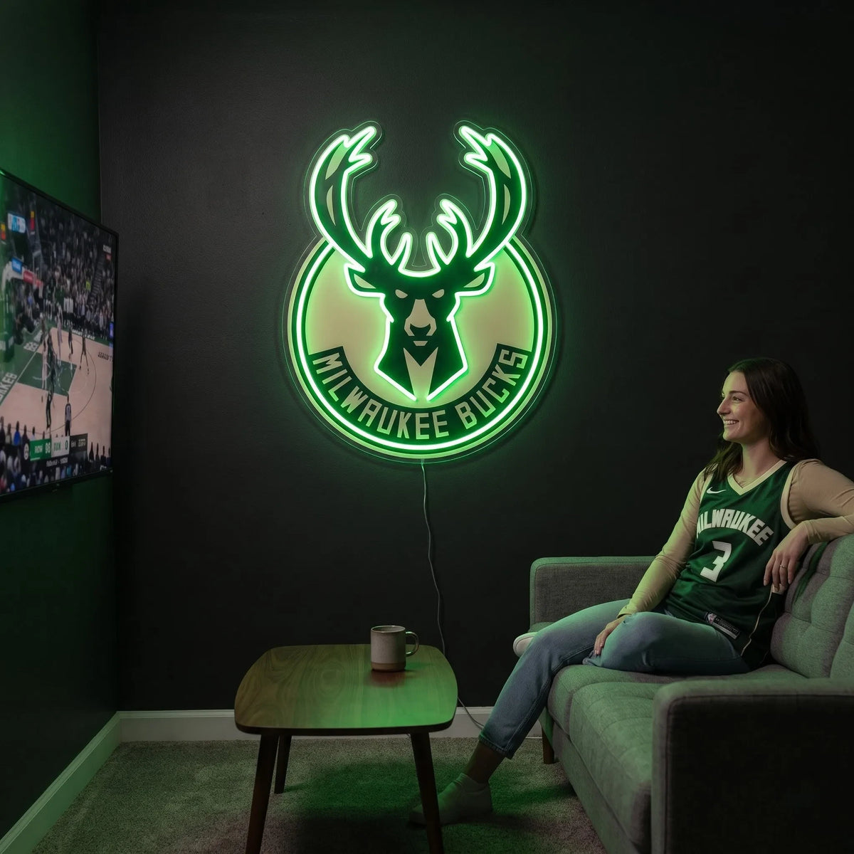 Milwaukee Bucks LED neon sign - A woman in a Bucks jersey relaxes on a couch beside a glowing green Milwaukee Bucks logo neon sign on a dark wall.
