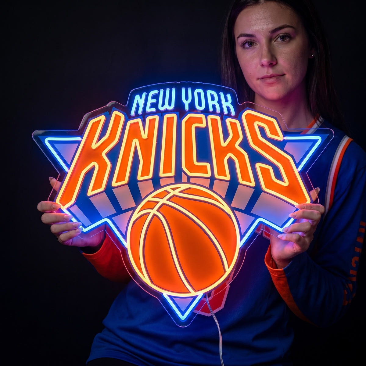 Woman holding a New York Knicks LED neon sign with orange lettering, a basketball and bright blue outlines