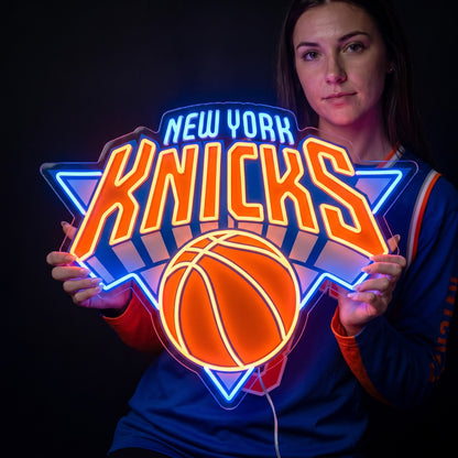 Woman holding a New York Knicks LED neon sign with orange lettering, a basketball and bright blue outlines
