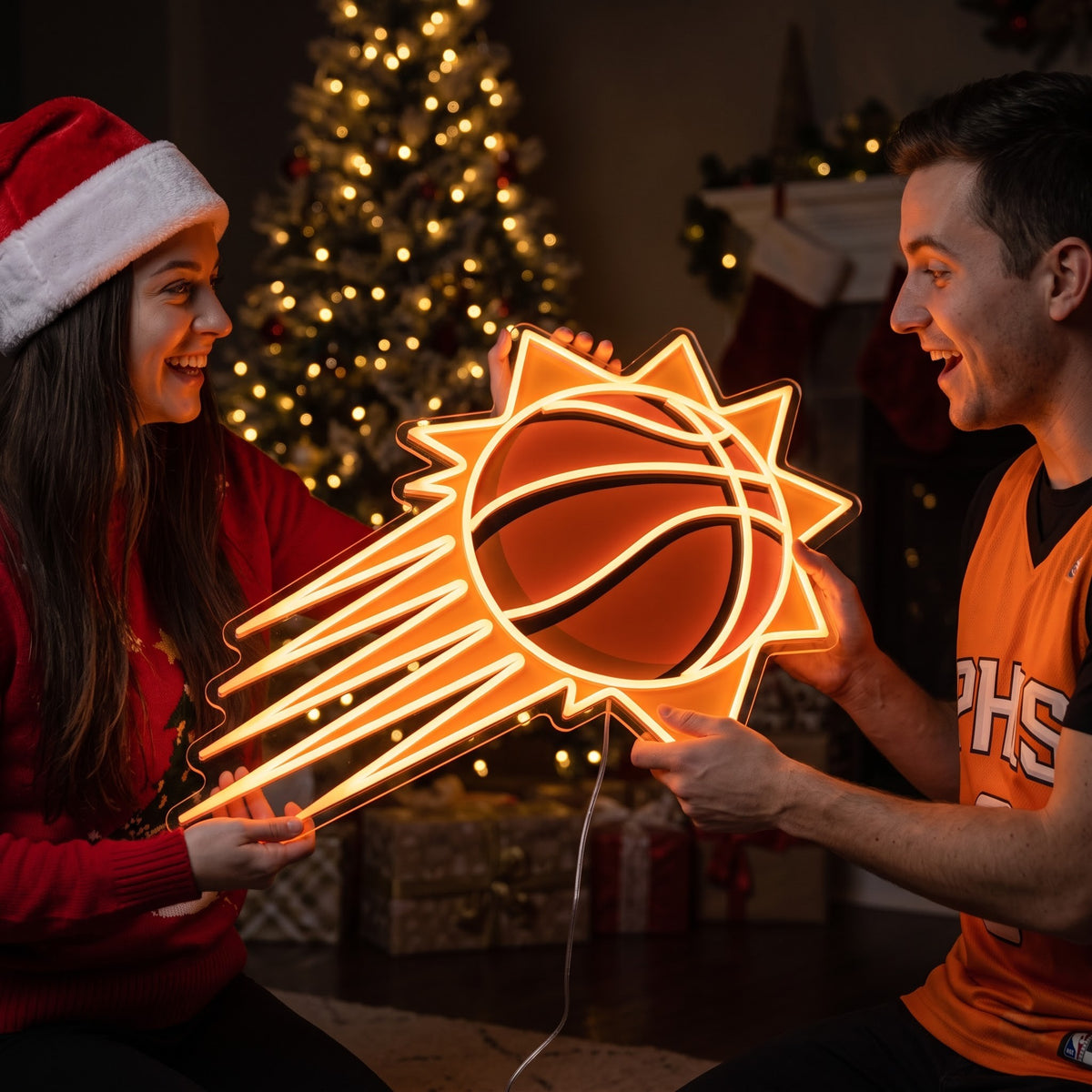 Couple exchanging a Phoenix Suns LED neon sign as a Christmas gift by the tree