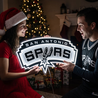 Couple exchanging a San Antonio Spurs LED neon sign as a Christmas gift by the tree