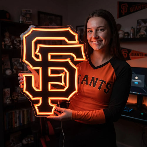 San Francisco Giants LED neon sign - A smiling woman in an orange Giants shirt holds a black and orange San Francisco Giants SF logo neon sign.