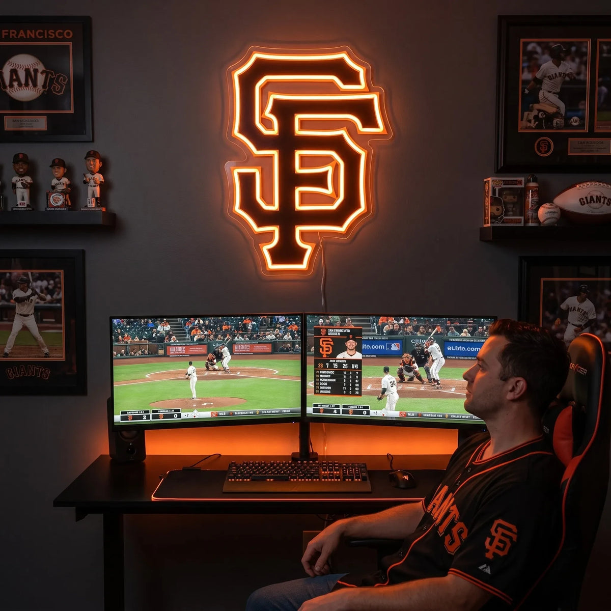 San Francisco Giants LED neon sign - A fan in a Giants jersey watches baseball on dual monitors under a glowing orange San Francisco Giants SF logo neon sign.