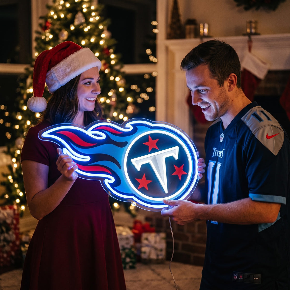 Couple holding a Tennessee Titans flame logo LED neon sign beside a Christmas tree.